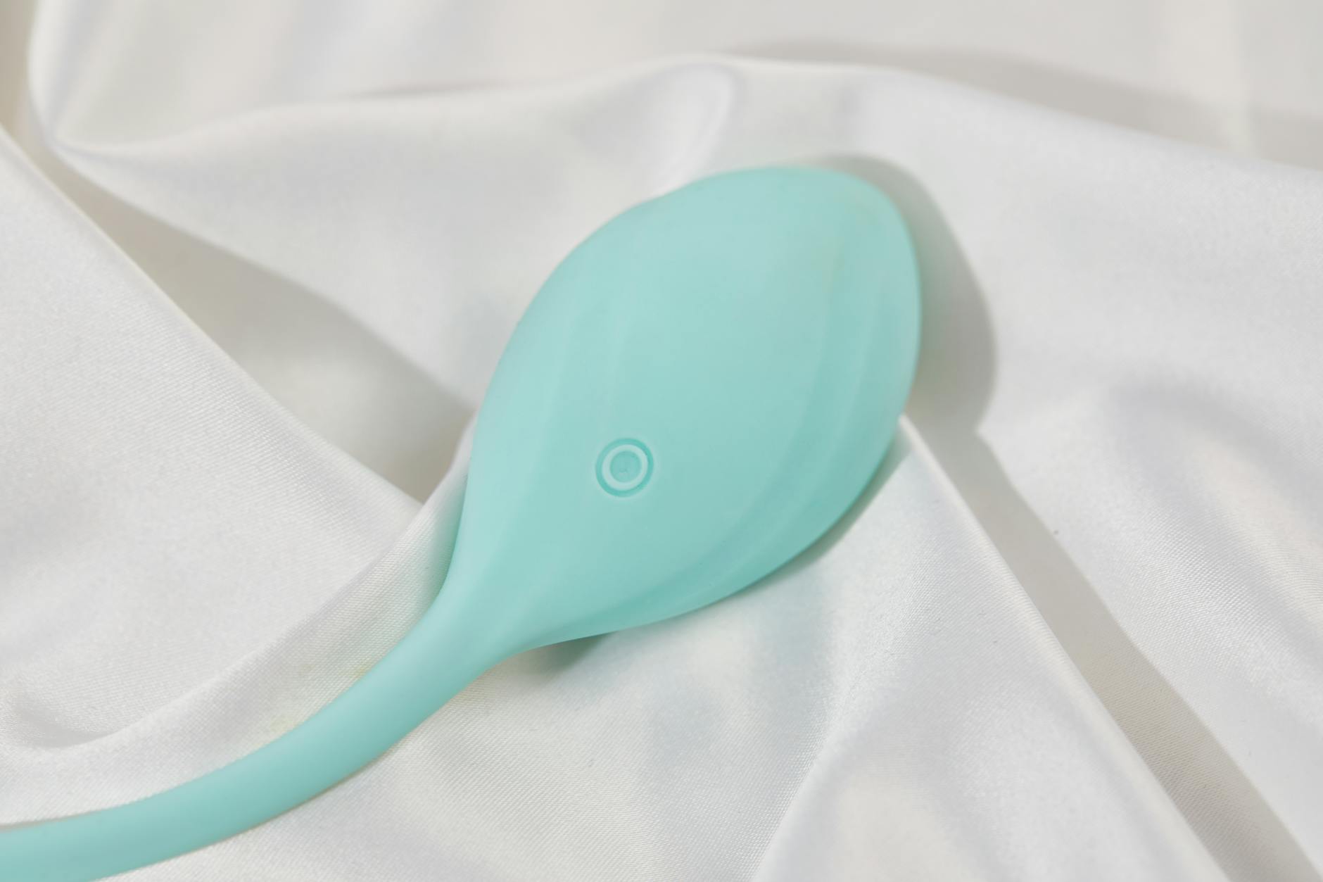 A teal lemon-shaped clitoral vibrator on white silk, symbolizing sensual pleasure and sexual wellness