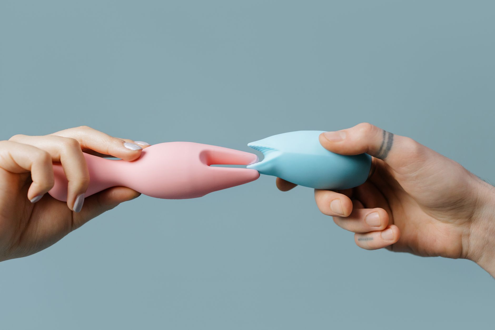Hands holding pastel-colored silicone vibrators, representing clitoral and intimate wellness tools for pleasure and pain relief