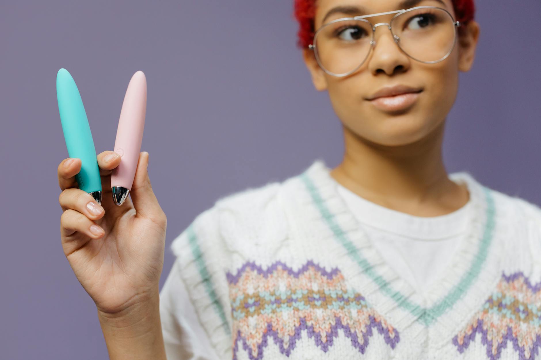 Woman holding colorful intimate wellness devices against a purple background, representing reconnection and intimacy restoration.