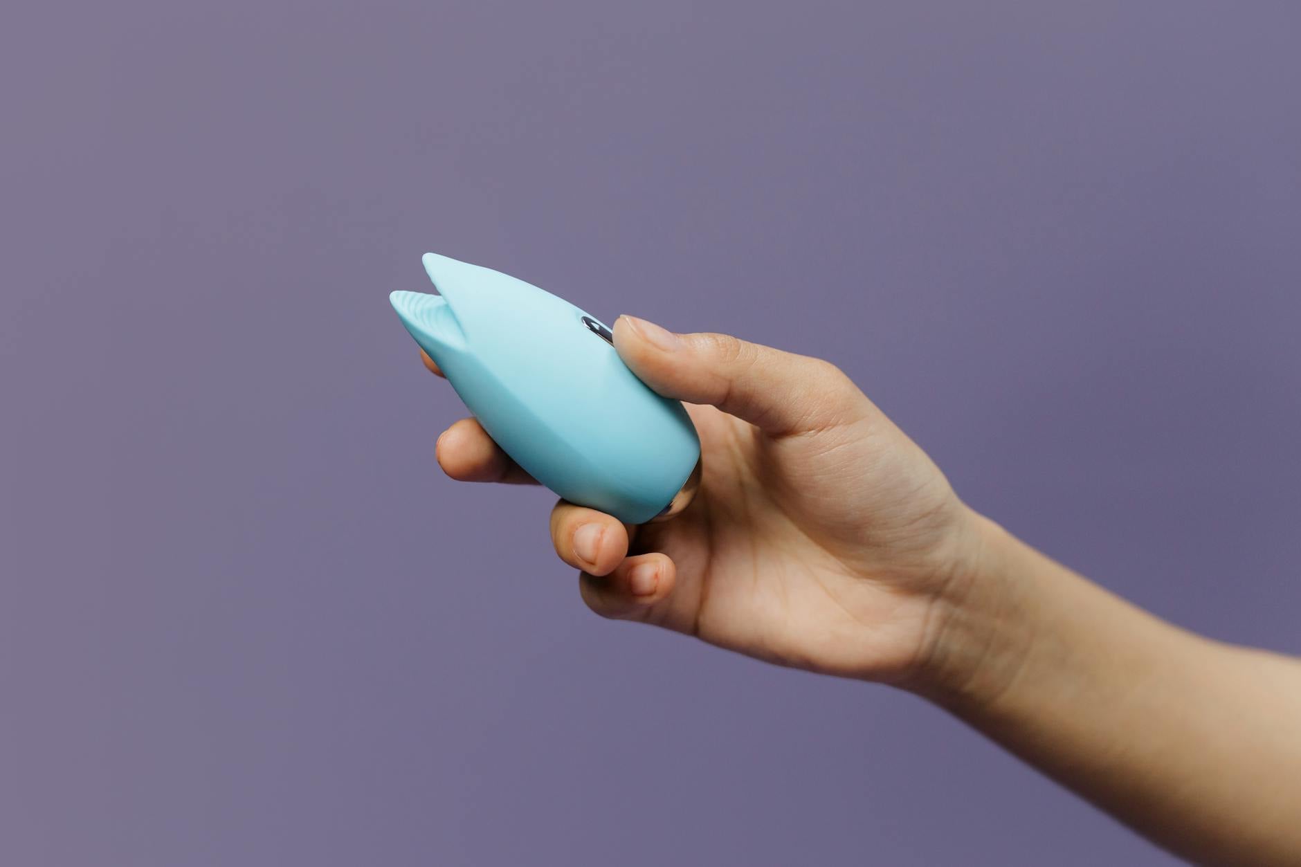 Two hands holding pink and blue silicone vibrators against a pastel background, representing shared pleasure