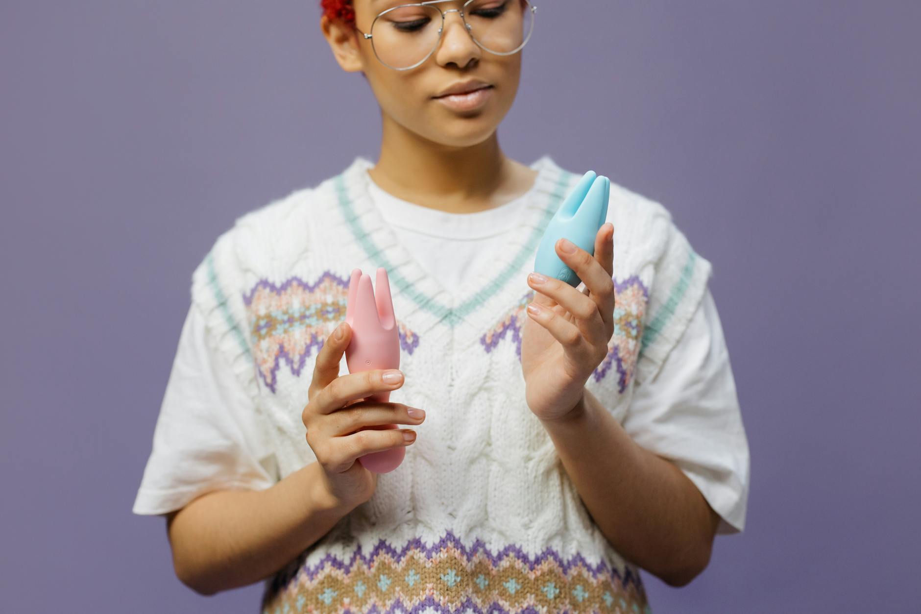 Woman holding pastel silicone clitoral vibrators in contemplative consideration