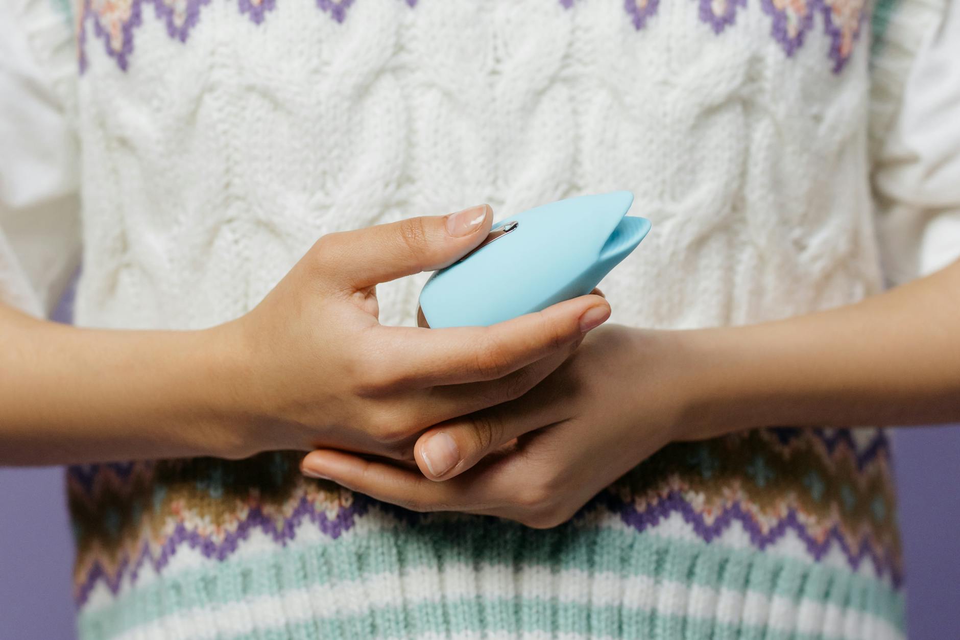 Intimate close-up of hands holding a sleek blue vibrator against a purple background