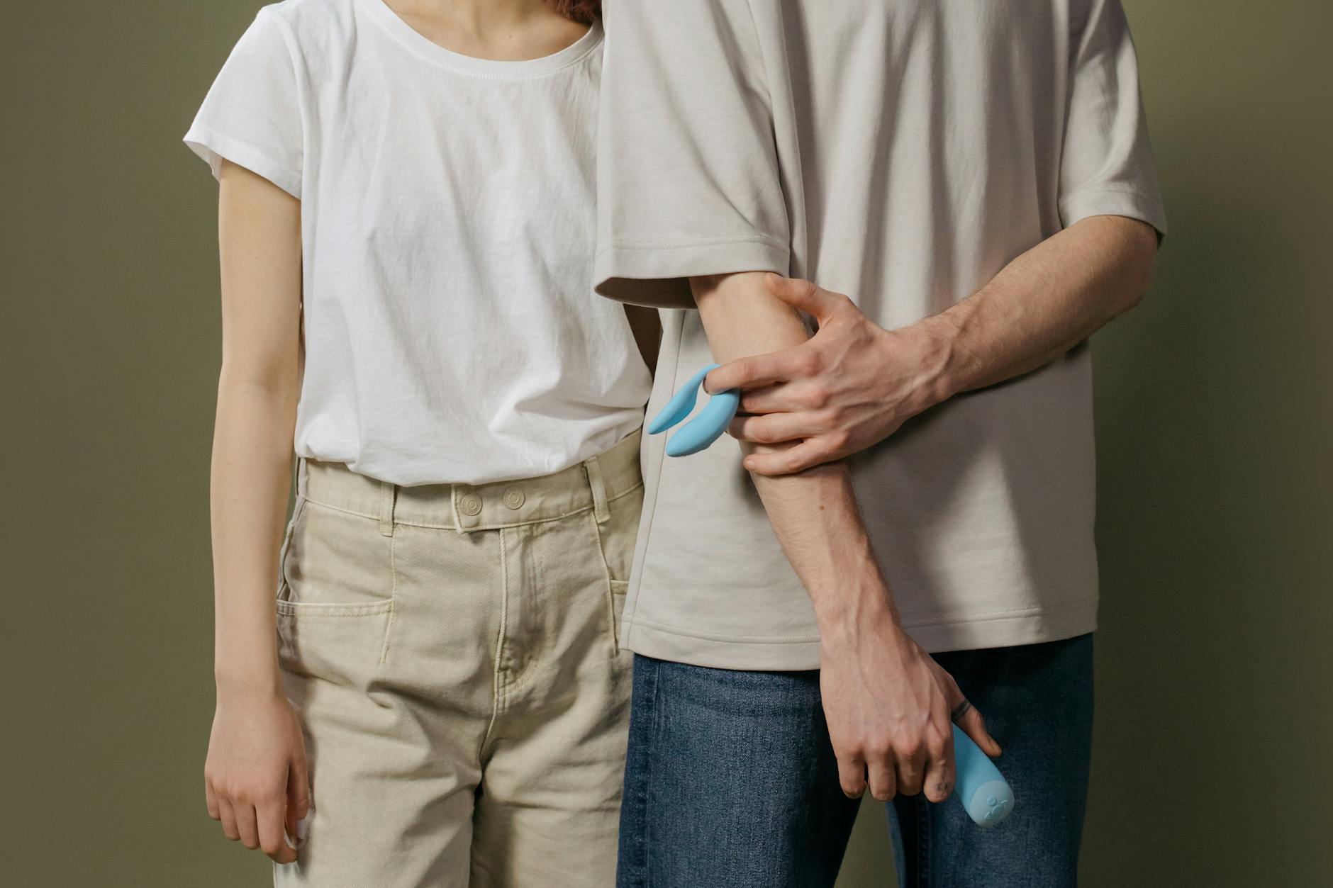 A young couple standing together indoors, holding a blue vibrator together, symbolizing modern intimacy and reconnection.