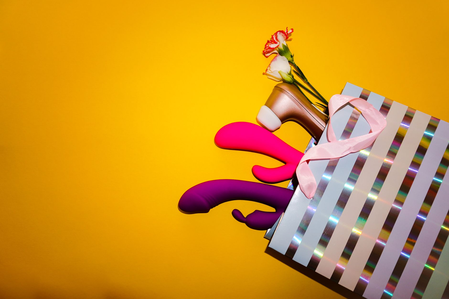 Colorful vibrators with flowers in a holistic gift arrangement against a bold yellow background.