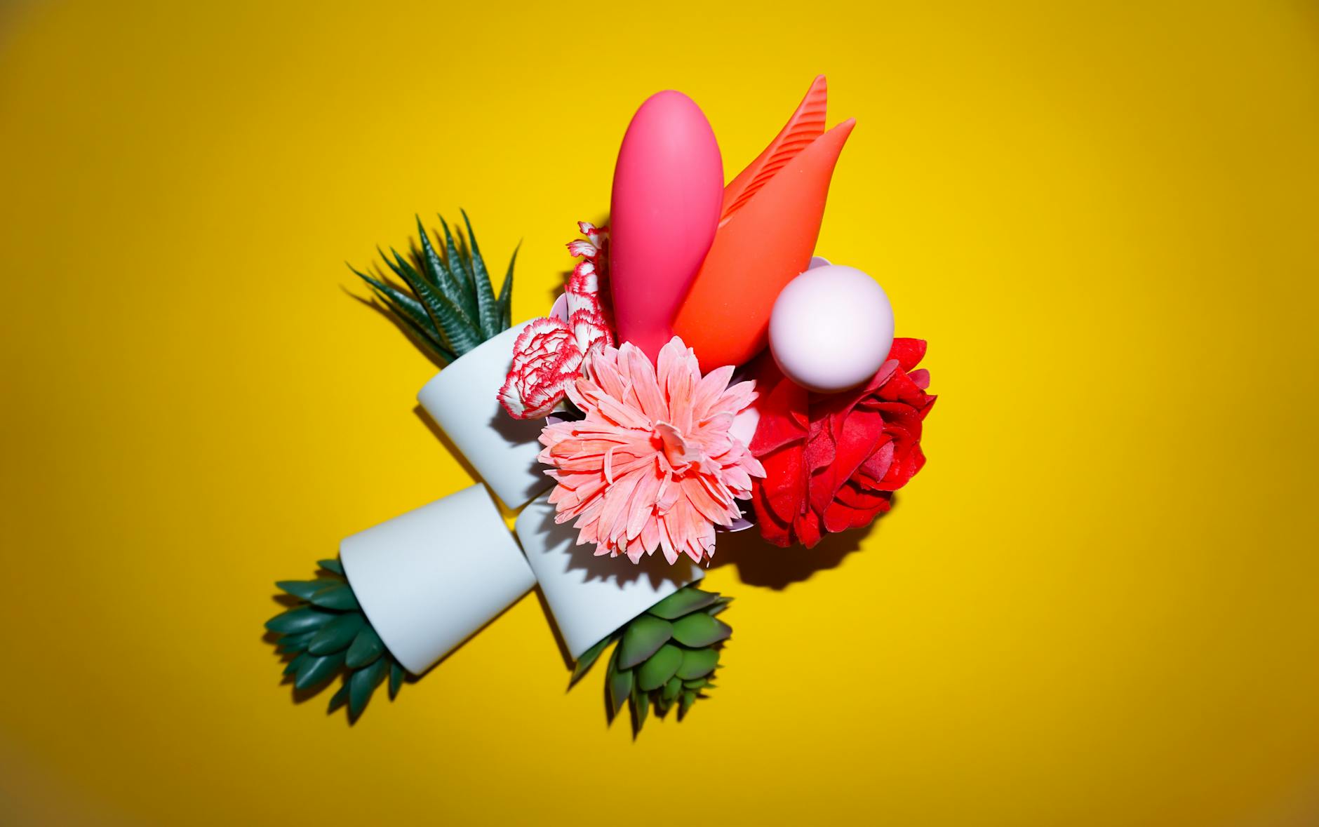 Two hands holding pink and blue silicone vibrators together against a pastel background