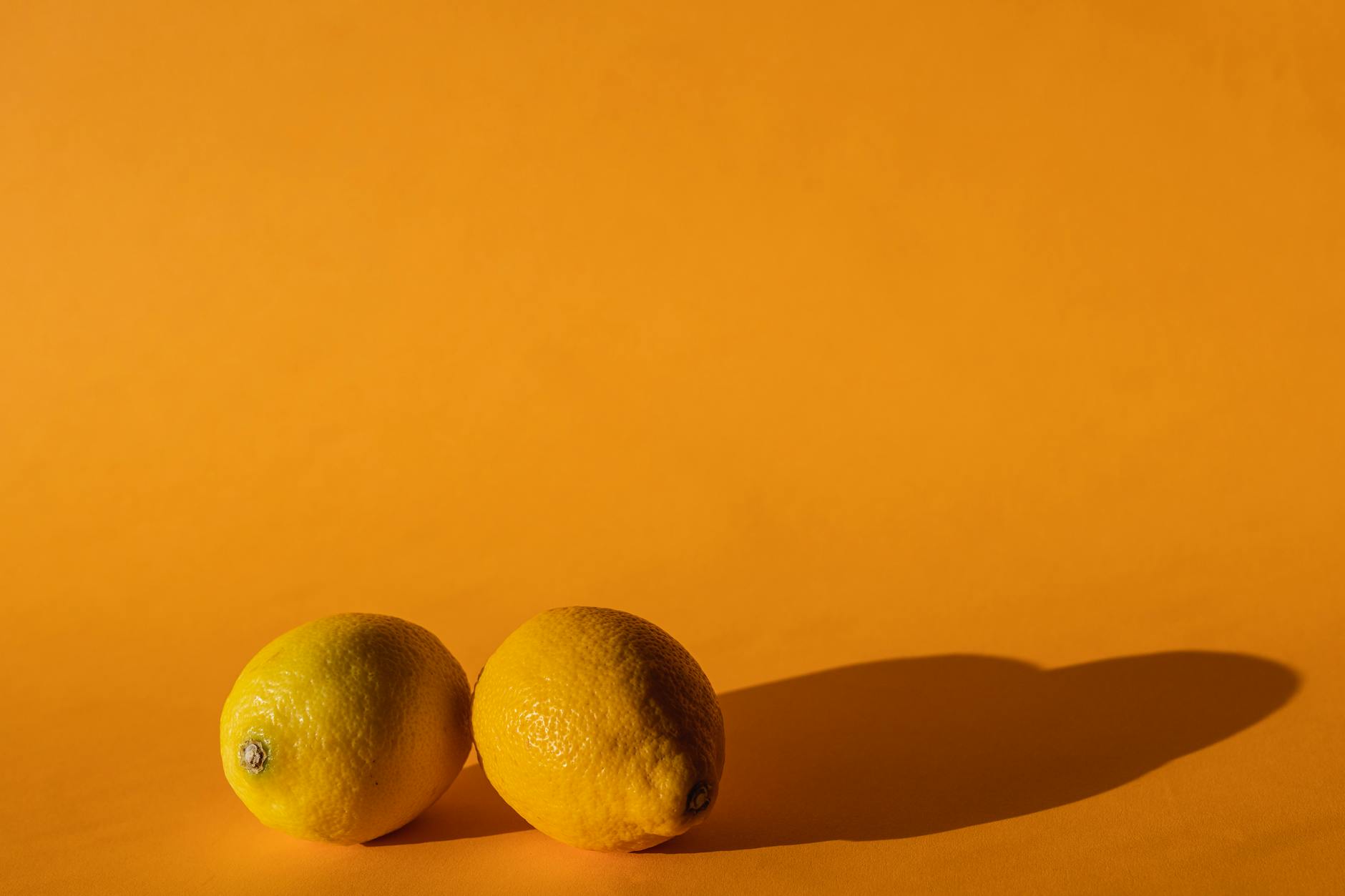 Hand holding a modern orange vibrator against a minimalistic purple backdrop